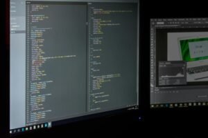 A dual screen setup showcasing programming code and image editing software.